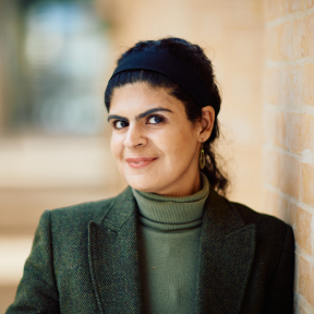 Minerva Singh standing in the Said hallway wearing a green suit and smiling. 