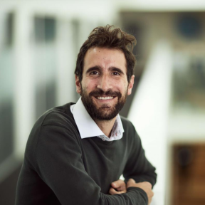 Paulo Savaget standing in the Said hallway wearing a grey jumper and smiling. 
