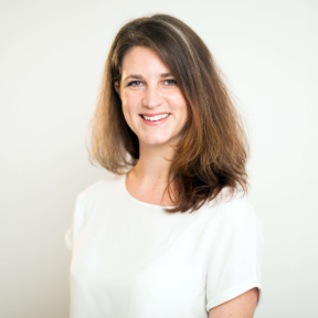 Pip Wheaton standing in front of a light background wearing a white top and smiling.