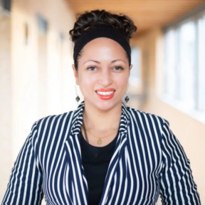 Tara Sabre Collier stood in an SBS hallway, smiling, and wearing a striped jacket. 