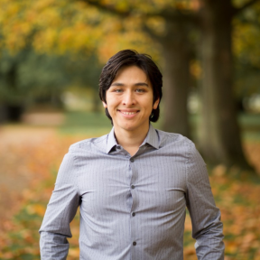 Alexander Wankel smiling in front of a leafy background. 