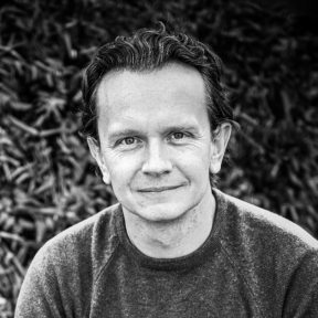Andy Thornton sitting in front of greenery smiling. 