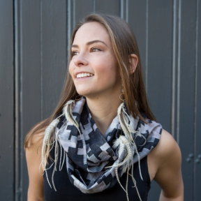 Anima La Voy wearing a grey scarf in front of an industrial building smiling. 