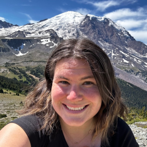 Ashley Thomas smiling in front of a scenic mountain landscape.