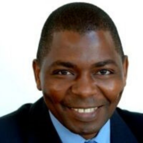 David Muhia sitting in front of a white background in a suit and tie.