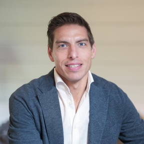 Derrick Feldmann wearing a pale shirt and grey blazer, smiling. 