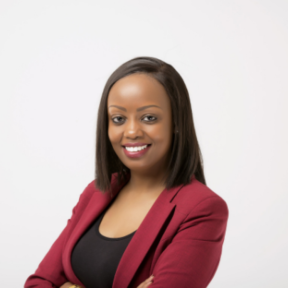 Diana Wangari is smiling in a crimson blazer and black top with her arms crossed, in front of a white background.