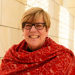 Gayle Peterson smiling in the Said Business School courtyard in the sun, wearing a red shawl.