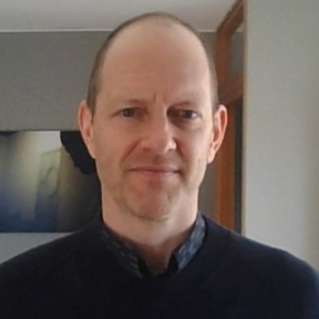 Jesse Fahnestock standing in front of a beige wall wearing a dark grey sweater.