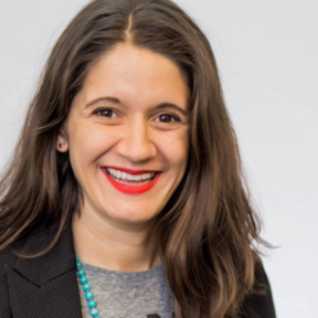 Jessica Shortall smiling in front of a grey background wearing a black blazer.