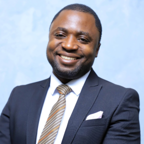 John Kakungulu Walugembe wearing a suit in front of a blue background.