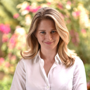 Jordyan Corcoran standing in front of a flowery background wearing a white shirt and smiling. 