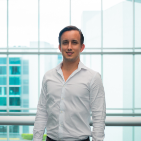 José Miguel Alfaro Gómez standing in a glass hallway wearing a shirt and smiling. 