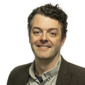 Kevin Warner smiling and wearing a brown suit. 