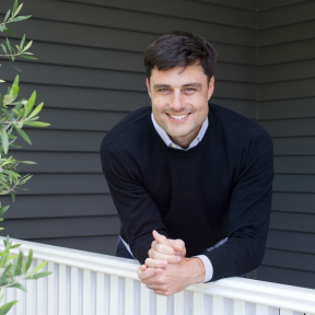 Louis Dorval leaning over a gate and smiling. 