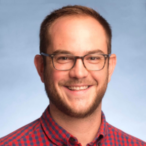 Mark Clayton Hand wearing a plaid red shirt and smiling. 
