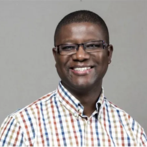 Martin Kalungu-Banda smiling in front of a grey background wearing a white, blue, beige and dark red checked shirt. 