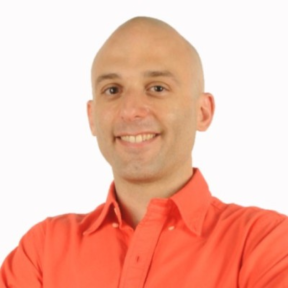 Nick Andreou smiling in front of a white background wearing a bright orange shirt.