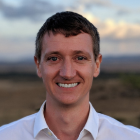 Patrick smiling at the camera in front of a wild landscape.