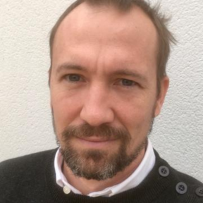 Rob Pettit standing against a white wall wearing a black jumper.