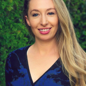 Sophie Maclaren smiling in front of a green hedge wearing a blue top.