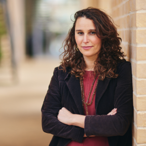 Laura Trajber Waisbich standing in the SBS hallway wearing a black blazer and red top.