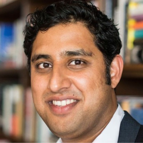 Rajiv Joshi smiling in front of a bookcase.