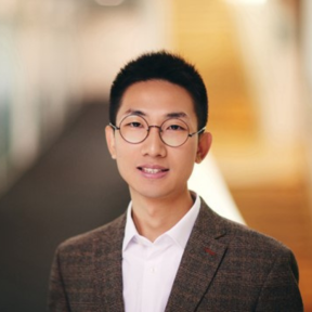 Cheng Li standing in the SBS hallway wearing a brown suit.