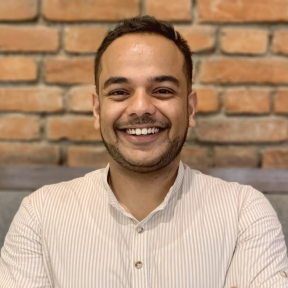 Achyut Gautam standing and smiling in front of a brick wall. 