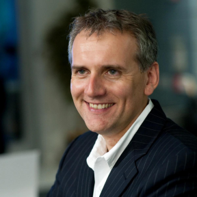 Sean Hinton smiling off to the side, wearing a dark navy suit. 