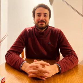 Sebastián Jaramillo wearing a red jumper crossing his arms and smiling at a desk. 