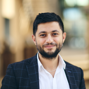 Closeup shot of Ammar in a white shirt and navy blazer, smiling at the camera
