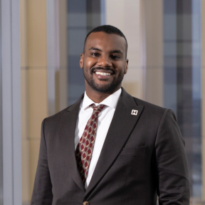 Yousif Yahya is smiling and wearing a suit in front of a building window. 