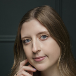 Close up headshot of Tori against a dark background. She is smiling and leaning slightly on her hand.