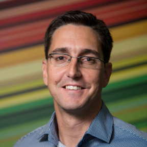 Francois is smiling in front a multicoloured background, smiling and wearing a light blue shirt. 