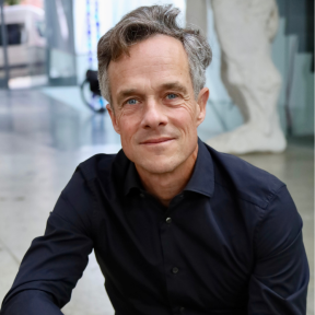 Sebastian is wearing a navy shirt and smiling. 